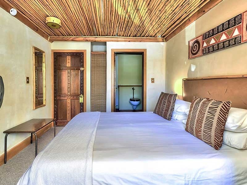 Bedroom with wooden ceiling, two beds, and a visible bathroom.